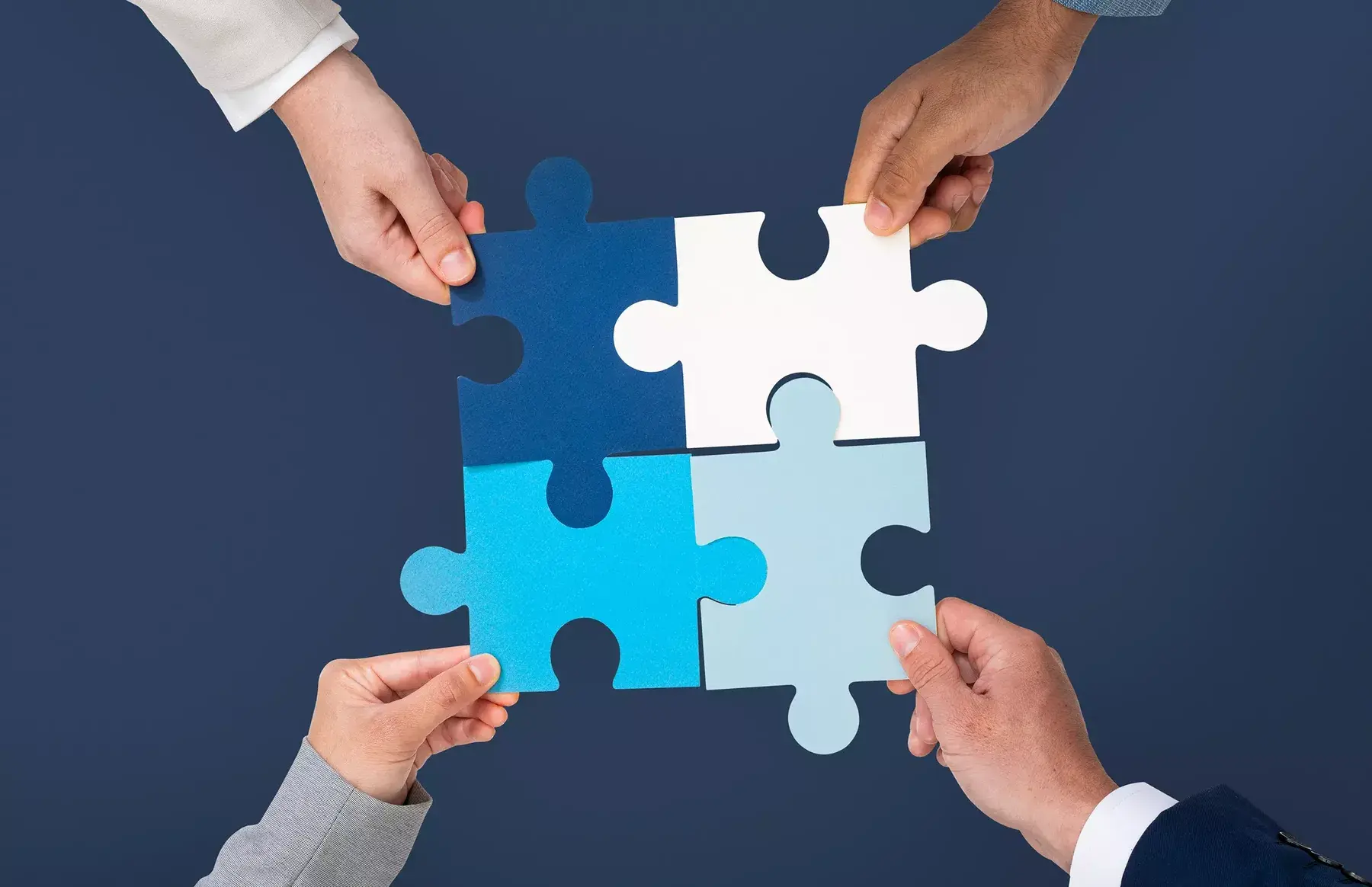 Four hands fitting puzzle pieces together, working as one team